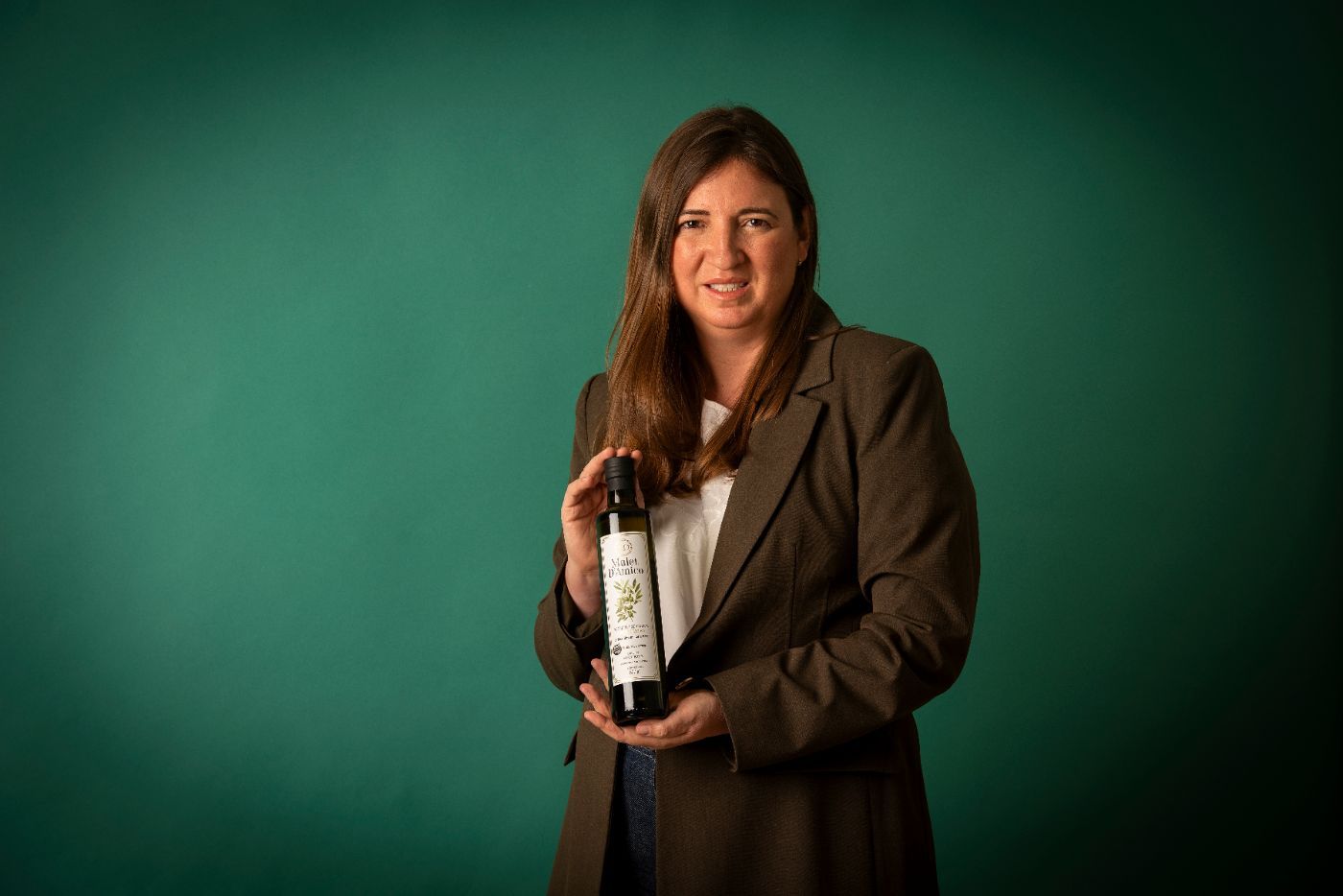 Lorena, cofundadora de Mulet D'Amico, sostiene una botella de aceite de oliva virgen extra frente a un fondo verde